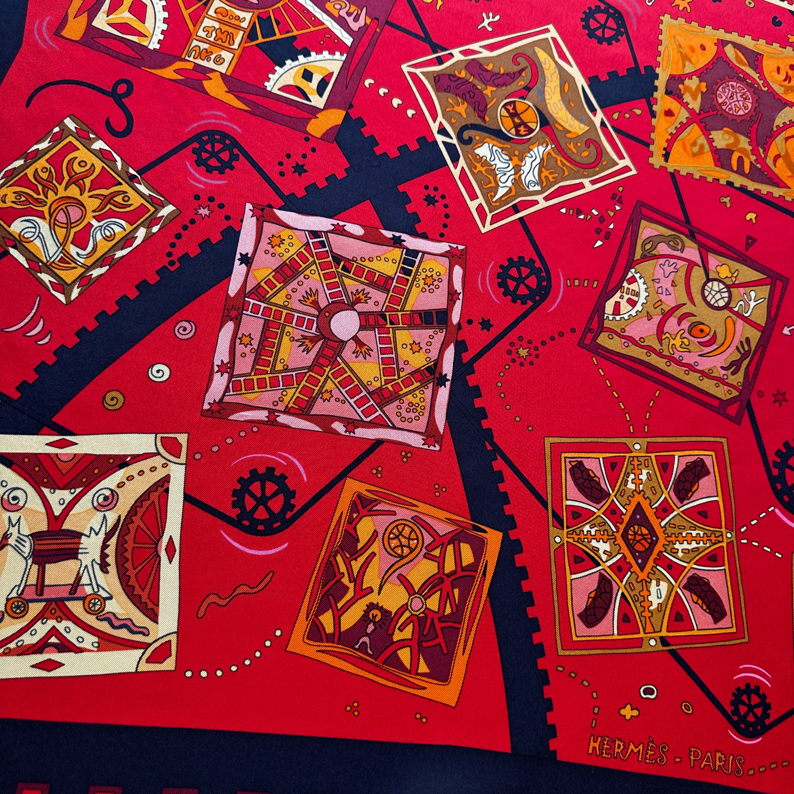 Détail des motifs de rouages et vignettes géométriques colorées sur fond rouge Hermès.