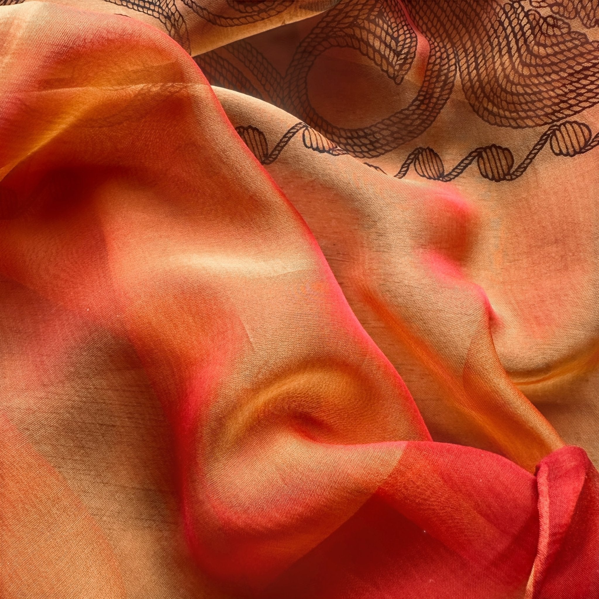 Gros plan de la mousseline de soie changeante du châle Hermès "Arabesques", montrant les reflets rouge orangé et or.