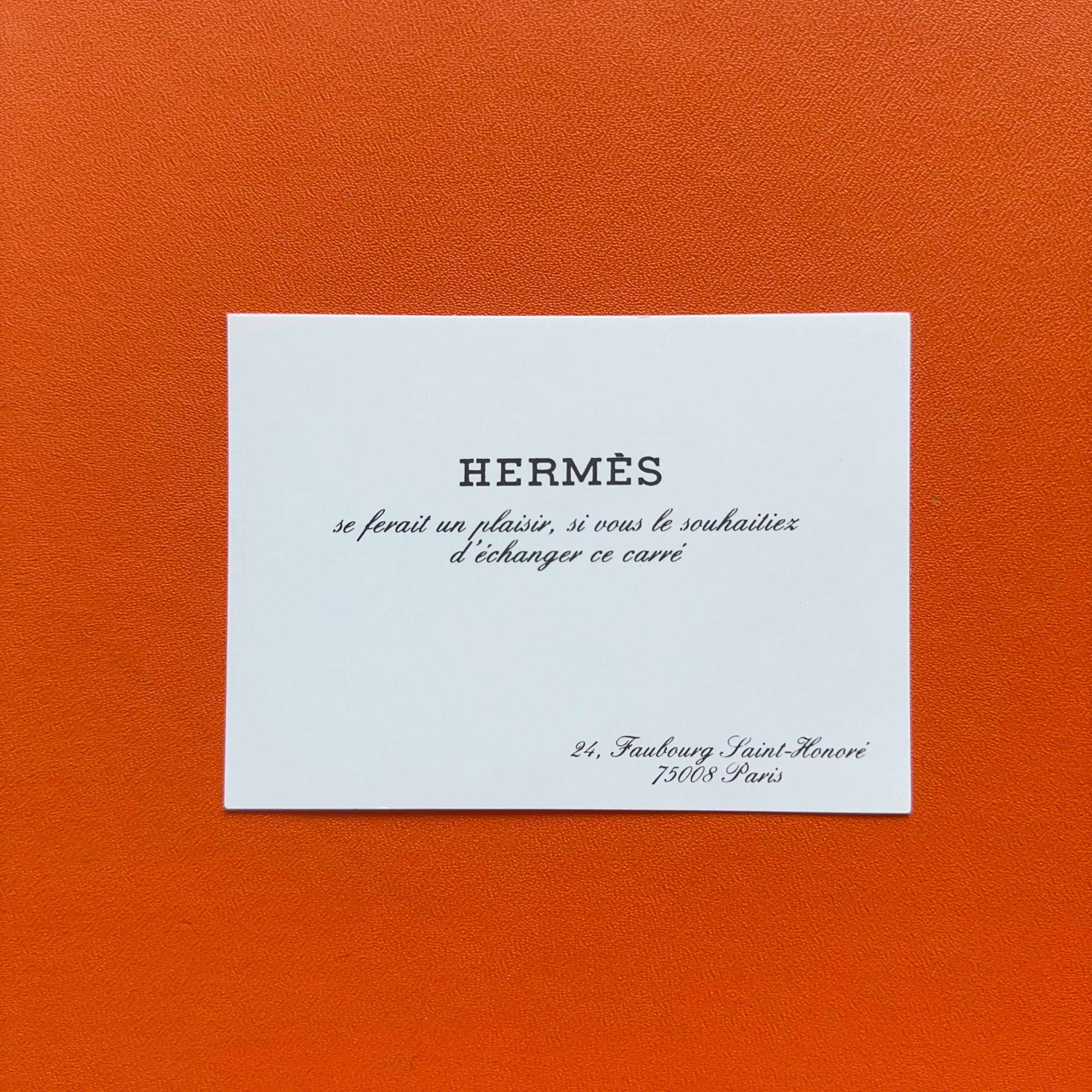 Gros plan sur la carte d'échange Hermès (carte Hermès cadeau vintage) posée sur le fond orange de la boîte.