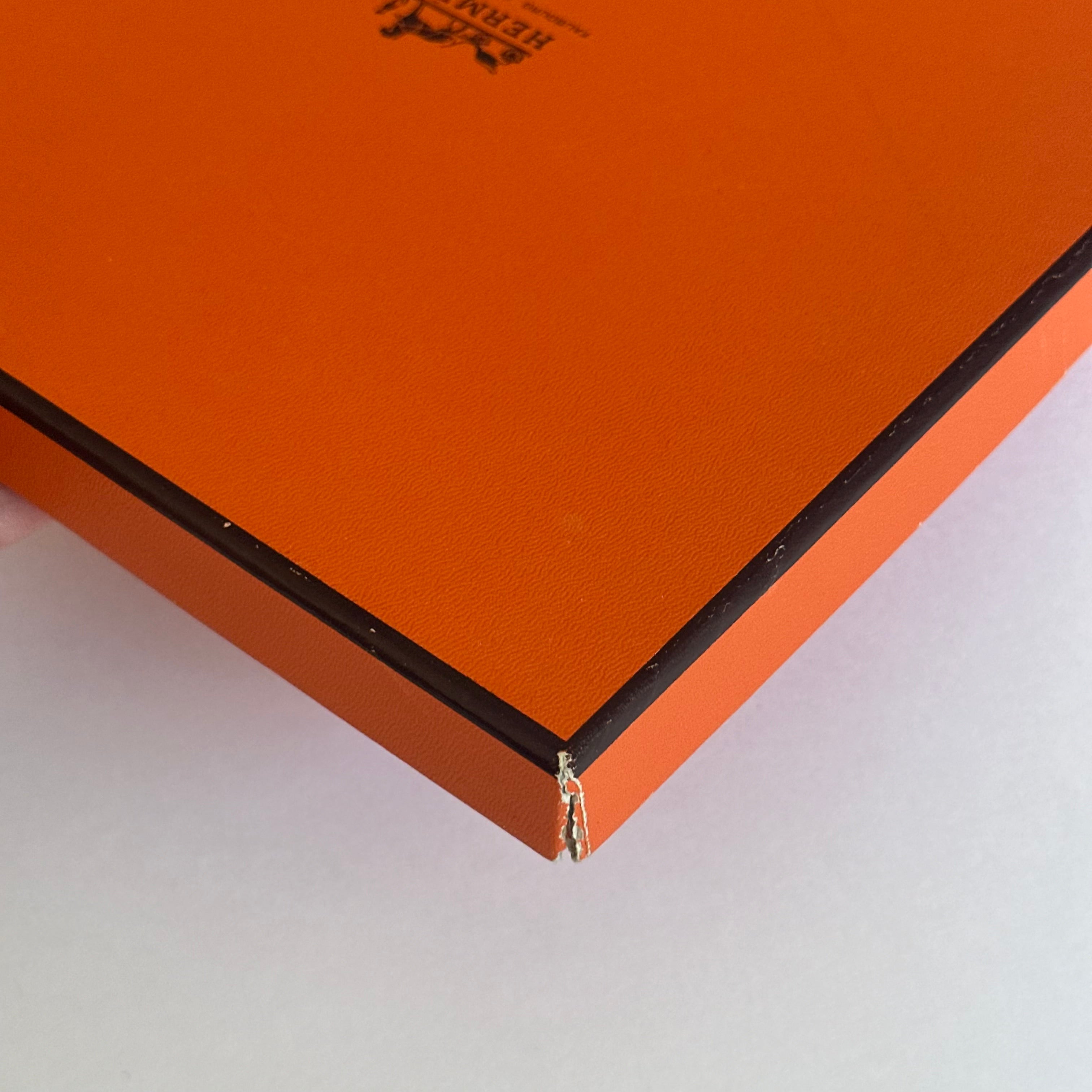 Vue rapprochée sur l'usure d'un angle de la boîte orange, montrant le carton blanc sous le revêtement texturé.