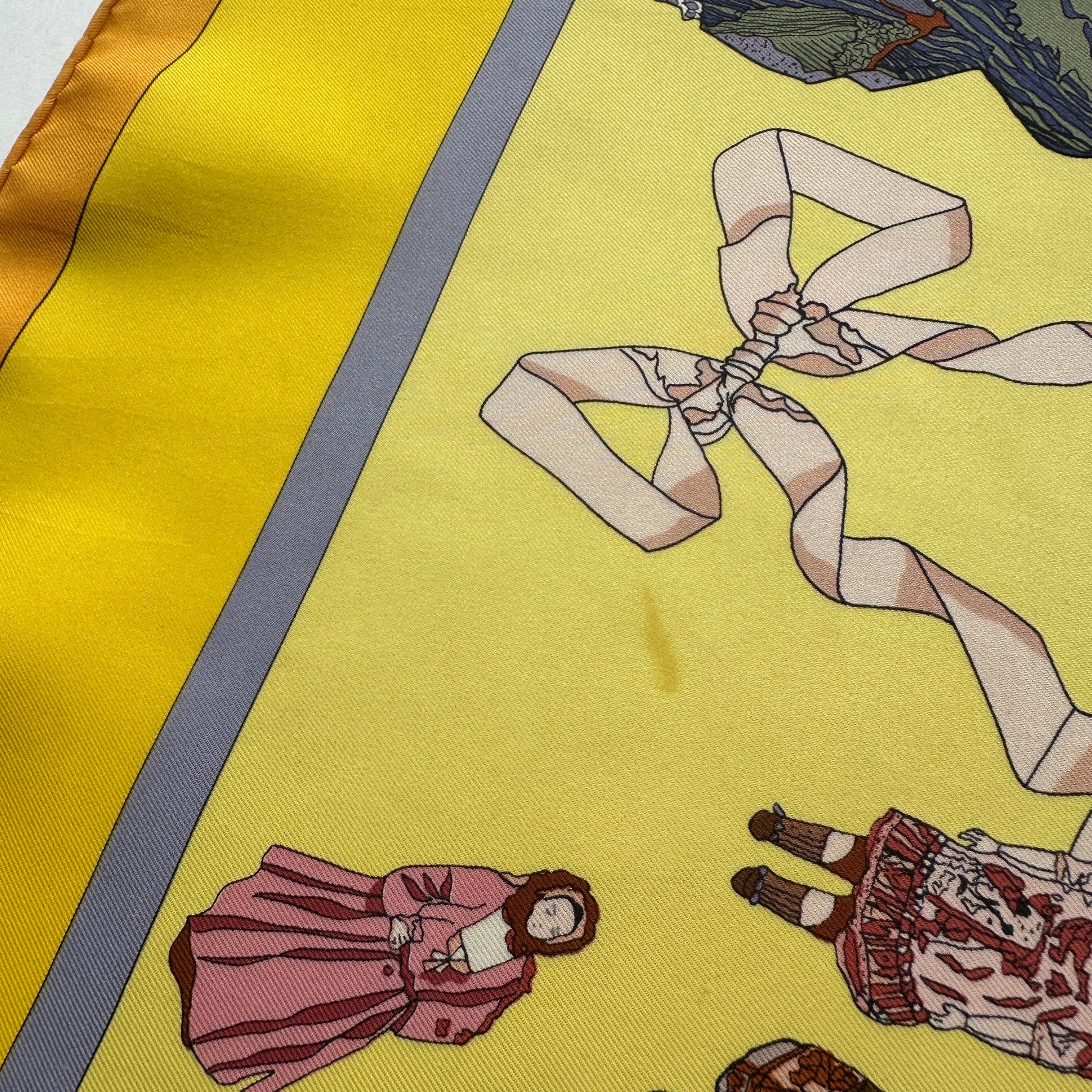 Gros plan signalant une légère tache visible sur le fond jaune du foulard, située à proximité d'un motif de ruban.