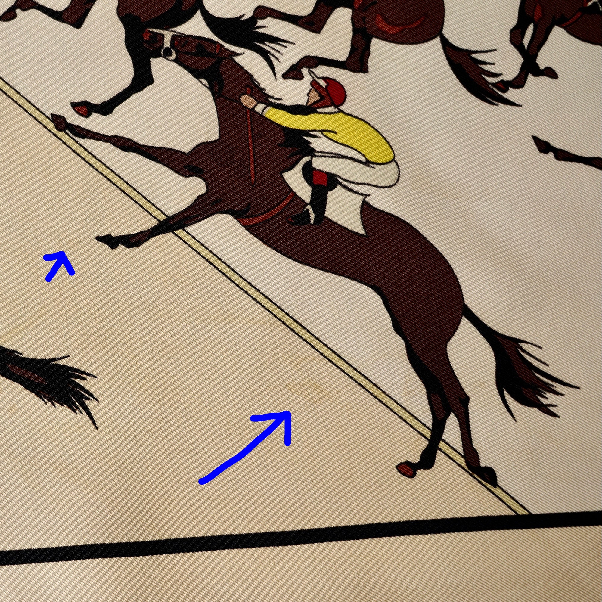 Zoom sur des petites taches discrètes sur le foulard Hermès "Les Courses", pointée par deux flèches bleues.